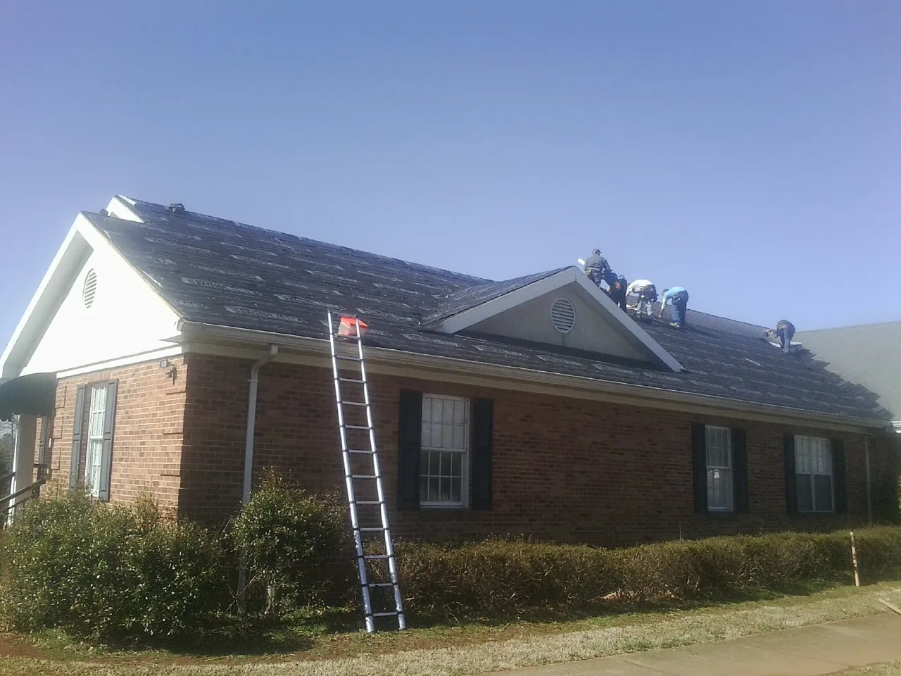 Crew tearing shingles off a brick ranch roof with a ladder set — Metal Roof Repair work by our crew in Climax