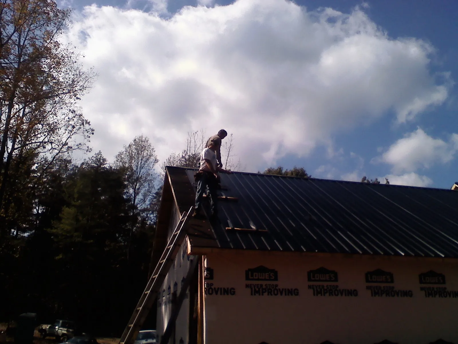 Roofer fastening dark metal panels high against a cloudy sky, from a Roof Inspection job in Climax